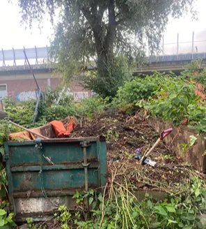 Vervuild terrein met opgehoopte planken, stoelen en afval vóór schoonmaak