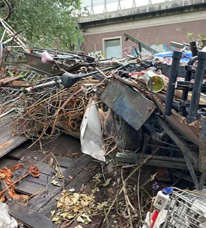 Een binnenruimte compleet gevuld met vuilniszakken, oude meubels en losse rommel; aan de muur hangen schilderijen.
