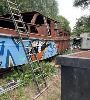 Buitenopslag van afval: houten platen, verhuisdozen, bankstellen en blauwe vuilniszakken liggen door elkaar.