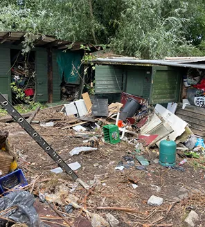Een enorme berg grofvuil en afval naast een gebouw; zichtbaar zijn plastic flessen, meubels, speelgoed en hout.