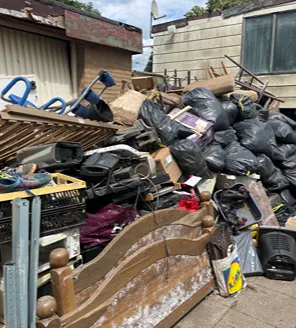 Een met afval bezaaid stuk braakliggend terrein met een dichte groene haag op de achtergrond, gelegen onder een viaduct.