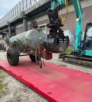 Een berg metaalafval en elektrische apparaten in een bosrijke omgeving, waaronder witgoed en gereedschap.