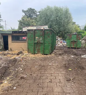 Een graafmachine tilt een roestige tank met grijper op, op een rode rijplaat onder een viaduct.