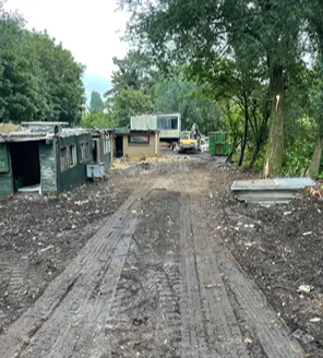 Een modderig pad tussen grote hopen afval. Links ligt een berg met grofvuil, plastic, hout en huisraad. Rechts zijn sporen zichtbaar van opruimwerkzaamheden.