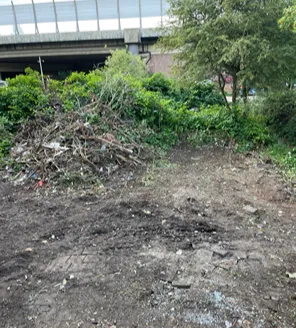 Een open plek met een hoop snoeihout en takken voor een geluidswal. De grond is grotendeels leeg en schoongeveegd.