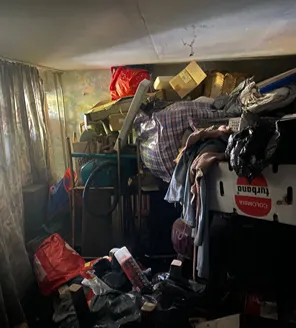 Binnenruimte volledig volgestouwd met huisraad, dozen en afval, waardoor nauwelijks bewegingsruimte overblijft.