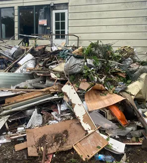 Grote berg grofvuil en puin tegen de gevel van een woning, inclusief hout, plastic en groenafval.