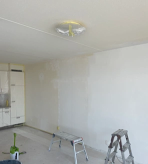 Van-gedateerde-woning-naar-instapklaar-appartement (8) Muur in renovatieproces met afgedekte lamp en begin van schilderwerk