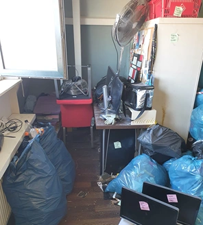 Grote stapel blauwe vuilniszakken in een woonkamer vol rommel en dozen.