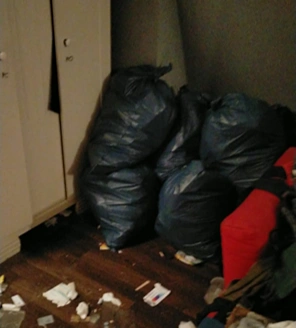 Donkere kamer met vuilniszakken in de hoek en rommelige vloer.