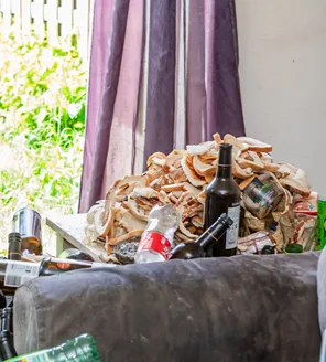 complete-transformatie-van-zwaar-vervuilde-woning-gallerij (12) Ophoping van schimmelige etensresten en drankflessen op tafeltje in woonkamer