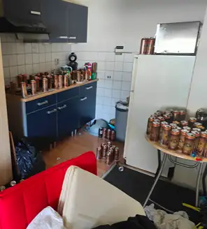 een-huis-opgeruimd-voor-een-frisse-start (8) Keukenruimte volledig bedekt met lege drankblikken en rommel.