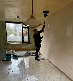nicotine-verwijderen-en-woning-ontruimen (2) Persoon in beschermende kleding bezig met het reinigen van het plafond met een stoomapparaat.