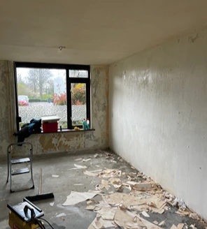 nicotine-verwijderen-en-woning-ontruimen (4) Grotendeels lege kamer tijdens ontruiming, met losgetrokken behang en puin op de vloer.