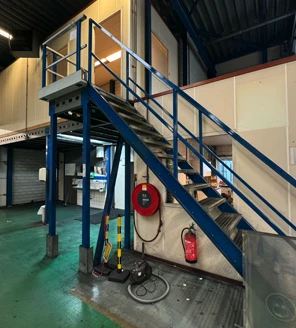 industriele-schoonmaker-trap-en-entresolvloer Een industriele schoonmaker zorgt voor een schone en veilige stalen trap naar een entresolvloer in een magazijn.