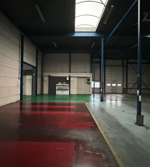 industriele-reiniging-magazijn-met-overheaddeur Magazijn met rood en groen geverfde vloerdelen die een specialistische industriële schoonmaak ondergaan.