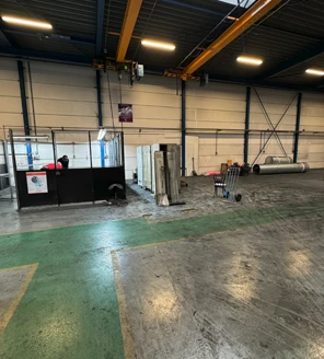 industriele-schoonmaak-bedrijfshal-voorbereiding Grote bedrijfshal met afgeschermde werkplek, klaar voor een grondige industriële schoonmaak door een professionele schoonmaker.