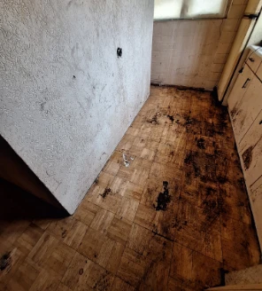 Lege keukenhoek na ontruiming met vervuilde houten vloer en aangetaste muur
