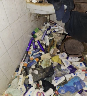 Detail van badkamer met vloer bezaaid met lege flessen en verzorgingsproducten