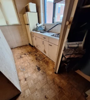 Leeggeruimde keuken met aangetaste vloer en zicht op aanrecht en koelkast