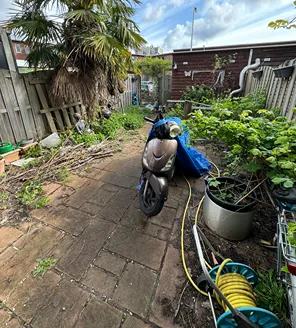 project-overwoekerde-tuin-gallerij (10) Tuin vóór de ontruiming, met scooter, overwoekerde planten en gereedschap verspreid