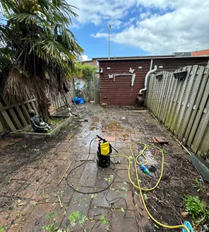 project-overwoekerde-tuin-gallerij (2) Tuin tijdens ontruiming, met gereedschap en hogedrukreiniger op het terras
