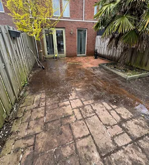 project-overwoekerde-tuin-gallerij (4) Tussenfase van het schoonmaken van de tuin met natte tegels en tuinslang zichtbaar