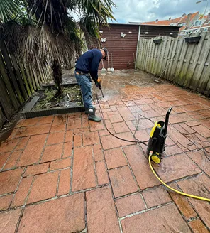 project-overwoekerde-tuin-gallerij (5) Man bezig met het schoonspuiten van het terras met een hogedrukreiniger