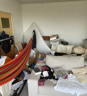 van-ontruiming-tot-verkoopklaar-maken (1) Woonkamer volgestouwd met dozen, kleding, een matras en een hangmat – klaar voor ontruiming.