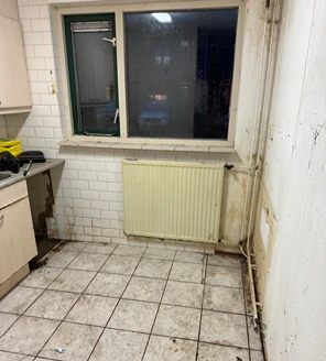 Schoongemaakte keukenhoek met tegelvloer en radiator na opruiming