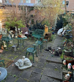 Verwaarloosde tuin met tuinbeelden, metalen stoelen en overgroei vóór tuinopruiming